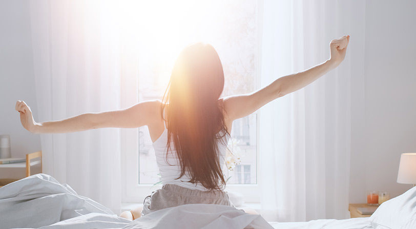 Photo of woman sitting up in bed and stretching