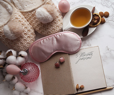 Picture of slippers, sleeping mask, relaxing tea, journal and candles
